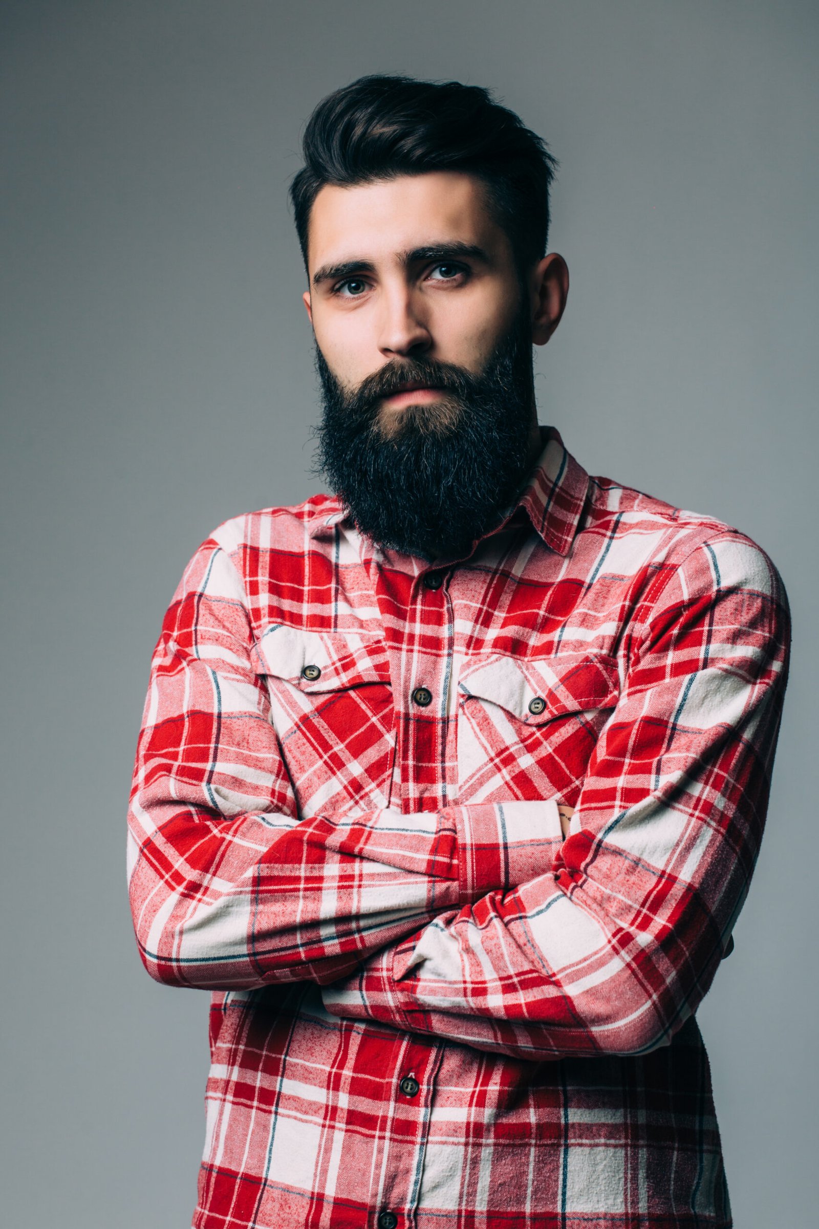 Portrait of masculinity. Portrait of handsome young bearded man looking at camera while standing against grey background